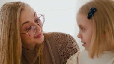 Kafkasyalı, gözlüklü anne, kapalı alanda konuşan 6 'lı yaşlarda bir kızla konuşuyor. Anaokulu çocuğu kız bebek ve anne bebek bakıcısı sohbet ediyorlar. Aile bağı güvencesi