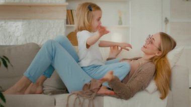 Kafkasyalı mutlu anne ve tatlı küçük kız sohbet ediyorlar oyun oynuyorlar kanepede uzanmış el ele tutuşuyorlar gülümsüyorlar anne evde küçük komik çocukla vakit geçiriyor.
