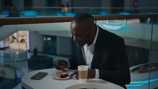 アフリカ系アメリカ人の中高年実業家の男性の訪問者はカフェテーブルに座ってパイを食べるおいしいケーキデザート親指を示す をジェスチャーを をレストランで満足お勧めします — ストック動画
