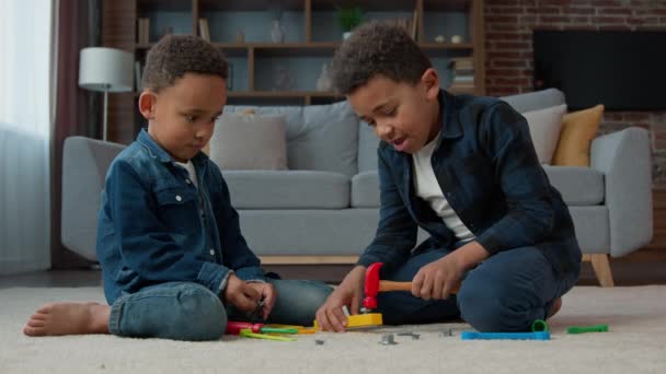 两名非洲裔小男孩非裔美国多种族儿童小学生坐在客厅的地毯上玩游戏 他们的亲兄弟朋友玩塑料玩具修理工具 — 图库视频影像