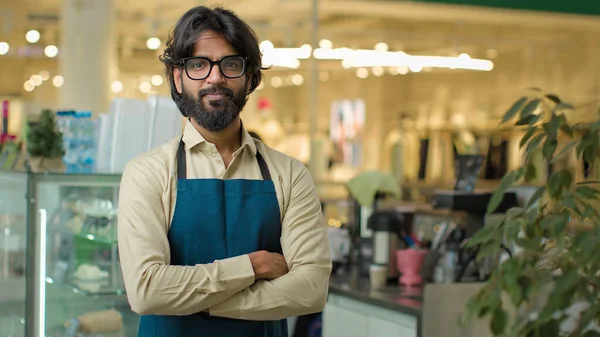 Successful small business owner bearded Indian Arabian man in eyeglasses standing in cafeteria restaurant showing ok gesture smile. Male cafe waiter worker guy with okay sign, good fine coffee service