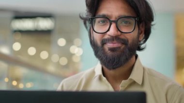 Happy confident Indian Arabian ethnic multiracial bearded businessman in glasses looking at camera in office, positive male employee man with laptop executive satisfied with good job career close up