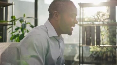 Mature African American ethnic middle-aged 40s man director businessman salesman sit at office desk morning sunshine day work with computer online surprise winning bet celebrate triumph yes gesture