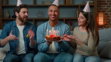 Multiracial people relatives family congratulate African american man with birthday presenting surprise sweet cake sing festive musical song diverse ethnic friends in funny caps blowing party whistles