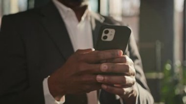 Cropped view male hands touch mobile phone screen typing message unrecognizable african american man adult office user businessman use internet web app close-up cellphone gadget in sun rays sunbeams