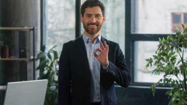 Smiling adult caucasian man in office look camera successful businessman professional manager entrepreneur showing ok sign approval gesture demonstrating support symbol excellent result recommendation
