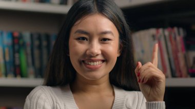 Portrait pensive korean woman standing in library near bookshelf think ponder deep in thought in search solution happy female comes up with good idea remembers make gesture raises finger finds answer