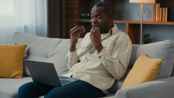 匿名アフリカ系アメリカ人の男性のクライアントは ラップトップを使用してビデオ通話で話している間にソファの上に座っている悪いサービス製品について不平を言うオンライン会議で怒っているビジネスマンの話不満を主張 — ストック動画