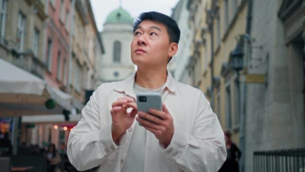 Zdezorientowany Koreański Mężczyzna Turysta Stojący Zewnątrz Trzymając Telefon Rozglądając Się — Wideo stockowe