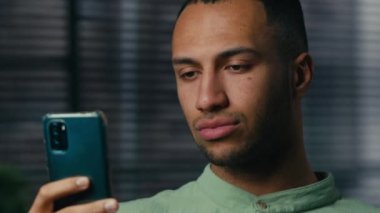 Close-up young serious african american businessman holding phone browsing social network checking email sad man reading news on internet on smartphone sending text message using mobile application