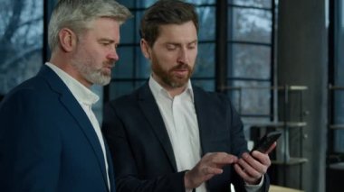 İki Kafkasyalı iş adamı ofiste konuşuyor genç erkek ajan satış danışmanı yaşlı erkek müşteriye danışarak sunum için cep telefonu kullanan iş ortakları iletişim kuruyor.