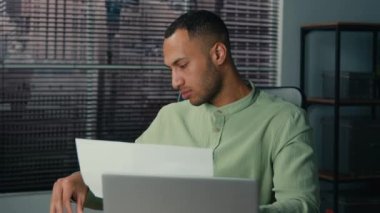 African american young businessman working in office looking through paper documents analyzing data check report doing paperwork ethnic man finance analyst reviewing financial statement in workplace