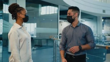 İki farklı meslektaş Hintli Arap erkek işadamı ve tıbbi yüzlü Afrikalı Amerikalı kadın iş kadını dirsek tokuşturma ile selamlaşıp ofiste dostça sohbet ediyorlar. Coronavirus kuralları.