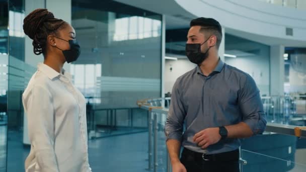 2人の多様な同僚インドのアラビア人男性ビジネスマンと医療面のマスクのアフリカ系アメリカ人女性がオフィスホールコロナウイルスのルールで一緒に優しい話肘バンプで挨拶 — ストック動画