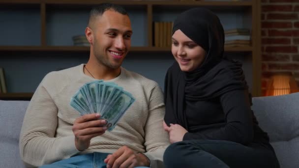 金持ちのイスラム教徒の女性とアフリカ系アメリカ人の男性の所有者は 現金ドル計画を保持します家族の予算は 宝くじ笑顔異人種間のカップルでお金を獲得金融住宅ローン住宅ローンのためのクレジットを受け取る — ストック動画