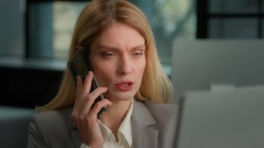 Caucasian female worker entrepreneur busy manager lady middle-aged serious woman with computer talking phone in office. Businesswoman talk with smartphone looking at screen speak with client distant