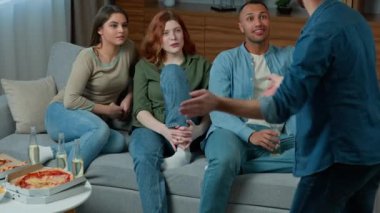 Group of happy diverse men women having fun play charades millennial guy showing pantomime riddles acting performing parody guessing interactive game at home multiracial ethnic friends guess personage