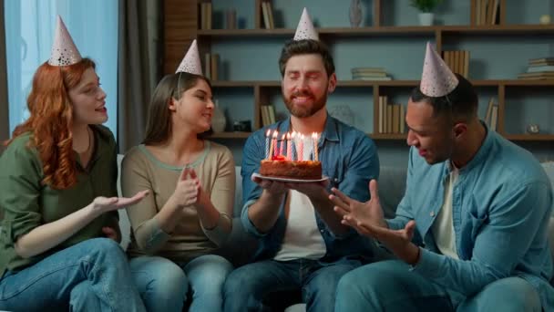 パーティーキャップの民族多様性のある女性と男性は男性を祝福します白人の友人は自宅でお祝いの歌を歌う幸せな誕生日の歌を歌う驚きのケーキを提示します — ストック動画