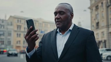 Yetişkin Afrikalı yetişkin erkek işçi yönetici girişimci orta yaşlı iş adamı şehir dışında telefon görüşmesi videosu ile ciddi iş görüşmeleri caddede uzak konferans sanal toplantıları