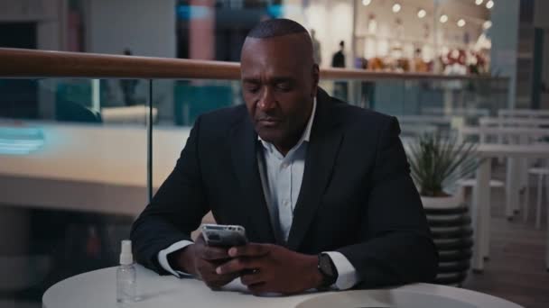 中世アフリカの成人男性社員カフェテーブルでビジネスマン起業家携帯電話の入力で買い物をするチャットテキストメッセージをオンラインでチャットスマートフォンとビジネスチャット — ストック動画