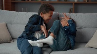 Happy two African American brothers friends little children boys siblings on home couch laughing playing fighting tickling. Affectionate cute funny kids having fun on sofa laugh together play tickle