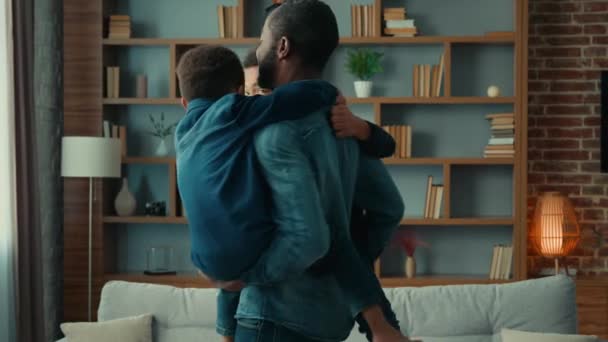 快乐的少数民族家庭在家里玩耍 非裔美国人的父亲抱着两个可爱的小儿子 抱着孩子们一起跳舞 在客厅里旋转着 在公寓里享受着有趣的周末 — 图库视频影像