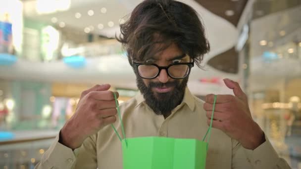 ショッピングモール内の袋の中を見て眼鏡でインドの顧客バイヤーの男性ショックを受けた反応不思議すごいカメラを見て言う驚いている アラビアひげそりクライアントビジネスマンオープン購入ギフト驚き — ストック動画