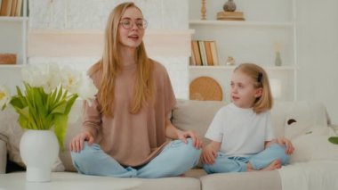 Küçük kızıyla birlikte beyaz bir anne Lotus pozunda evde oturmuş meditasyon yapıyor ve konuşuyor. Gözlüklü anne, anaokulu çocuk meditasyonu öğretiyor. Gözleri kapalı oturup birlikte meditasyon yapıyorlar.
