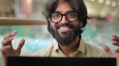 Happy excited Indian worker man in glasses celebrate business success online winning good result with laptop looking at camera smile. Arabian bearded businessman executive with computer achievement