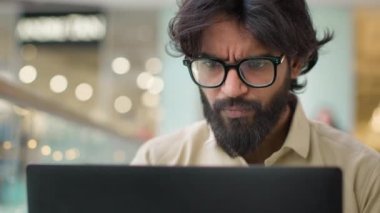 Ciddi Hintli gözlüklü bir adam laptop ekranına bakıyor ve içeride çalışıyor. Gözlüklü Arap işadamını kapat bilgisayar yöneticisiyle sohbet et iş mali verilerini internetle analiz et