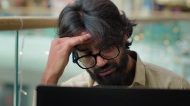 Dizüstü bilgisayarlı üzgün Hintli iş adamı endişeli iş problemleri baş ağrısını evde hisseder. Bilgisayarlı Arap sakallı işçi yönetici iflas etti.