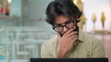 Concentrated pensive thoughtful Indian worker man in glasses hold rubbing chin think about business online problem with laptop. Arabian bearded businessman with computer thinking idea ponder solution