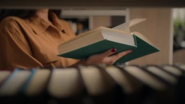 Close-up unrecognizable woman reading book in library female student teacher standing near bookshelf turning page textbook reads fiction preparing for university exam studying next to shelves books