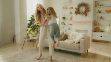 Caucasian mother lift raise little 5s daughter holding child girl baby carefree dancing together singing in living room. Loving mom carrying kid enjoy weekend leisure dance to music enjoy motherhood