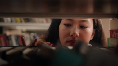 Close-up young asian woman browsing shelves books concentrated female student looking for necessary book to read on bookshelf searching right textbook to prepare for exam search literature in library