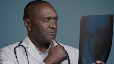Yakın çekim Afro-Amerikan erkek doktor, tramatolog, radyolog, stüdyo mavi arka plan, röntgen taraması sonucu tomografide iyi niyet göstergesi var.