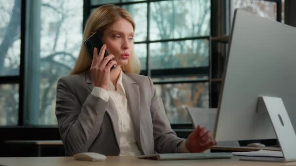 マルチタスク女性オフィスワーカーコンピュータトーク携帯電話を入力する白人の中年の大人の女性は ビジネス取引マルチタスクを議論します オフィスのビジネスマンはオンラインで働くスマートフォンと話しています — ストック動画