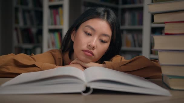 退屈悲しい疲れた怠惰な若い韓国人女性は大学図書館の机の上に横たわる退屈な本を読んでやる気のない女性学生は勉強と大学試験の過負荷のために準備をしています愛情のない科目 — ストック動画