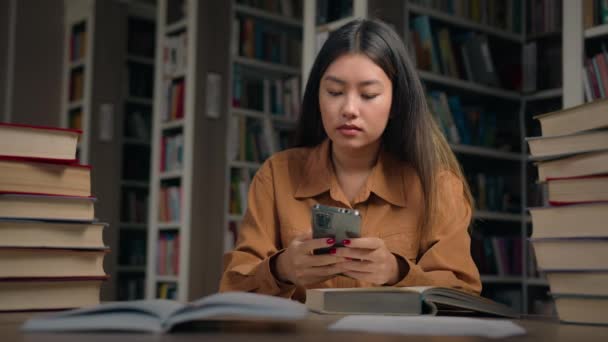 Genç Ciddi Asyalı Kız Öğrenci Kütüphanede Oturmuş Internetten Bilgi Topluyor — Stok video