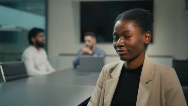 アフリカ系アメリカ人の成功したビジネス女性の満足度の高い女性マネージャーの労働者がオフィスに座っている同僚のぼやけた背景を持つカメラを見て親指を示す良いアイデアサポートビジネスプロジェクト — ストック動画