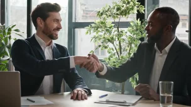 オフィスのデスクでは 多様な多人種間のビジネスマン多民族のパートナー男性握手 白人のセールスマン銀行経営者がアフリカ系アメリカ人顧客を銀行融資保険契約で握手 — ストック動画