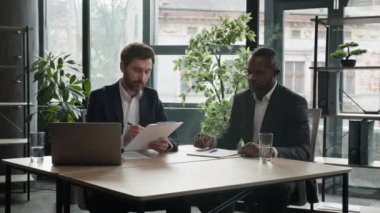 Multiethnic Caucasian and African American business people diverse multiracial men two male partners sitting at office desk sign document corporate paper successful partnership deal signing contract