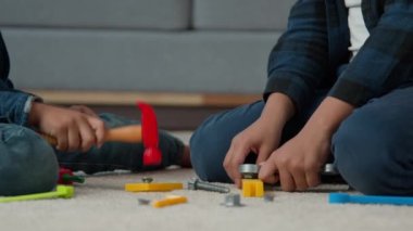 Close-up unrecognizable African American children kids boys friends sons play with plastic toys repair tools hit nail with hammer unscrew bolt nut with wrench play mechanic builder at home on floor