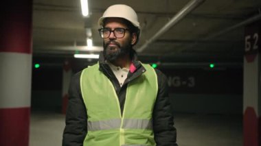 Profesyonel endüstri mühendisi, Hintli, gözlüklü, sakallı, güvenlik üniformalı, kasklı adam. Otopark endüstrisi uzmanı fabrikada çalışıyor, etrafa bakınıyor.