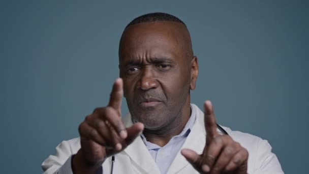 スタジオでアフリカ系アメリカ人男性医師青の背景ジェスチャー空中タッチ架空のホログラム画面を介して手を動かす驚きの男性は 将来のデジタル技術を使用して診断を調べる患者を分析 — ストック動画