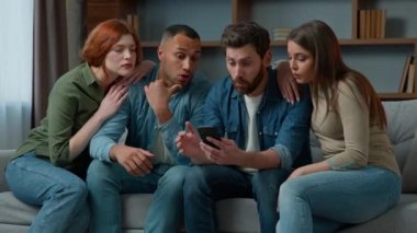 Surprised 30s middle-aged women men consumers read good news on mobile phone cellphone diverse ethnic friends multiracial people using virtual app smartphone indoors win business offer victory fortune