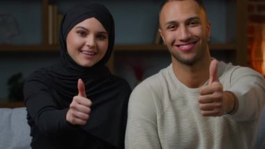 Olumlu ırklar arası çift, yeni evliler, etnik ev sahipleri, tesettürlü Müslüman kadın ve afro-amerikalı erkek evde oturuyor. Ev kredisi tavsiyesi gibi el hareketlerini onaylıyorlar.