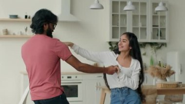 Excited couple funny dancing moving to music in modern kitchen dance motion together arabian hispanic man and woman in love active girl guy dancers celebrating relocation day at new home rented house