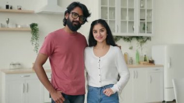 Portrait of two people multiracial couple in love posing in domestic white kitchen. Arabian hispanic indian ethnic family partners married woman and man spouses homeowners hugging at home apartment