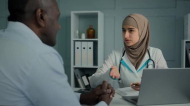 Medical consultation in clinic female doctor cardiologist arabian woman give professional advice to sick patient old man write prescription notes in notebook filling health insurance writing diagnose